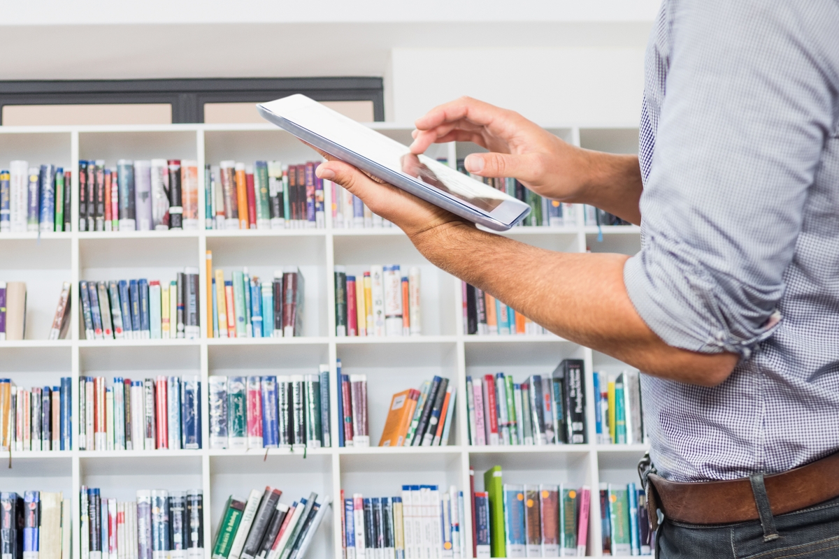 Composite image of man holding digital tablet with library background